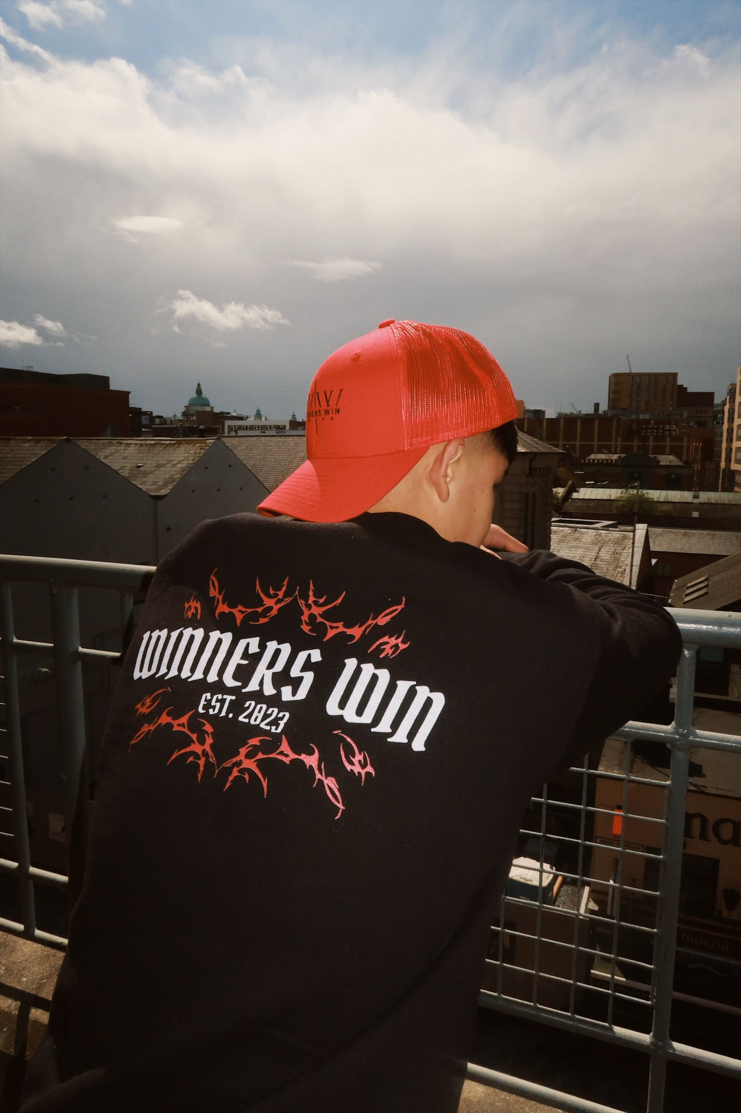 The model is wearing the Winners Win graphic sweatshirt while looking over Belfast city centre